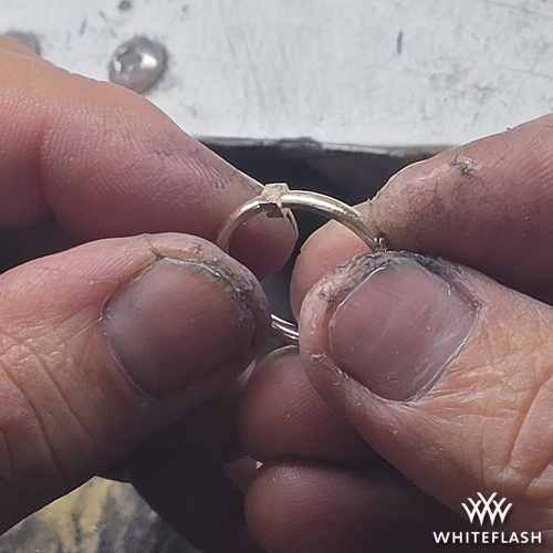 A jeweler holding a ring with a newly added section of metal, carefully ensuring a precise fit before soldering and finishing the resizing process. The hands show the detailed craftsmanship involved in seamlessly enlarging the ring.