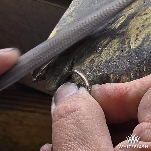 A jeweler carefully filing down a resized ring on a workbench, smoothing the newly added section of metal to ensure a seamless finish. The craftsmanship is evident in the precision and attention to detail.