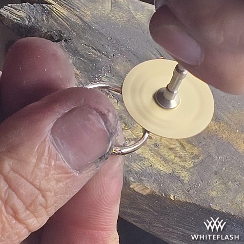 A jeweler using a rotary tool with a sanding disc to smooth and refine the resized section of a ring. The high-speed sanding process ensures a seamless transition between the original band and the newly added metal.